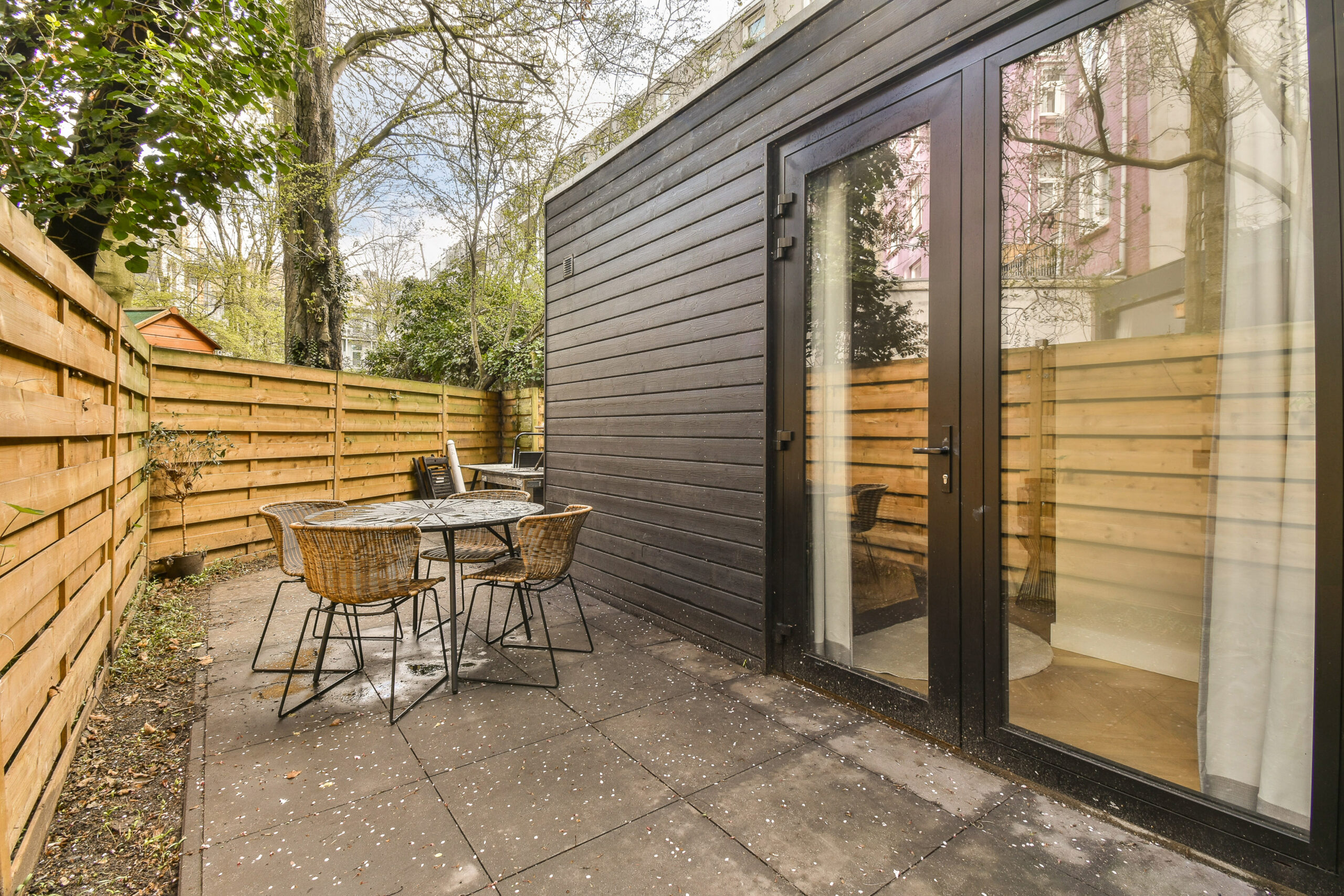 a patio with tables and chairs in front of a wooden fenced backyard area that is surrounded by green trees