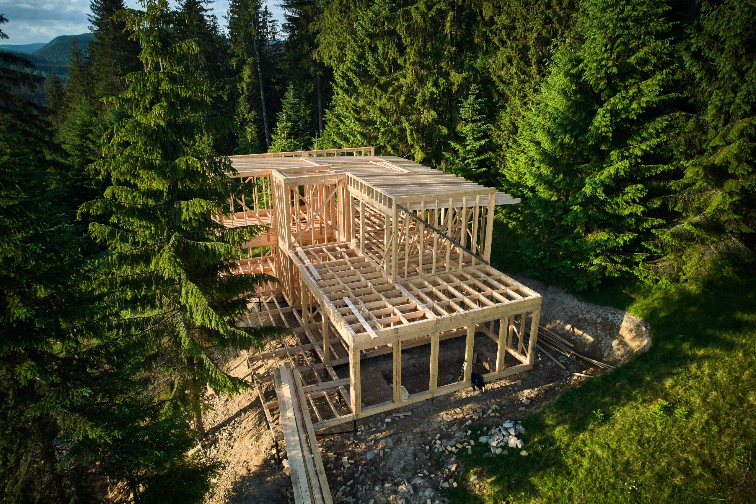 Drone view of two-story wooden frame house under construction near forest. Idea of modern ecological construction and contemporary architectural design.